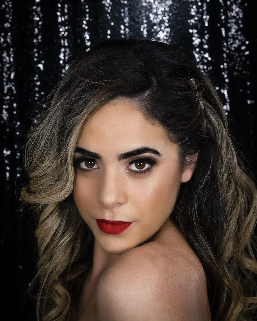 Glam makeup with a classic red lip and soft waves against a black sequin backdrop, by Lips and Lashes by Yane